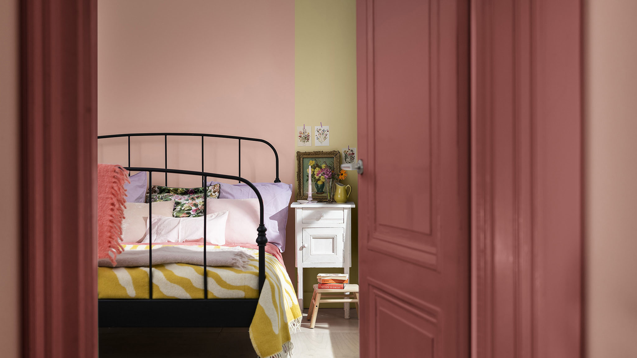 Looking through a door into a bedroom with a vertical split wall in pink and straw-yellow.