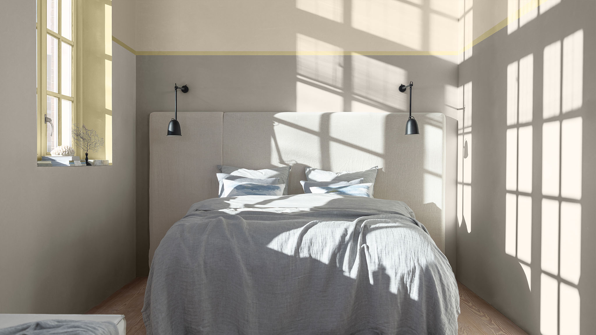 A bedroom with a painted split wall effect and straw-yellow around the window.