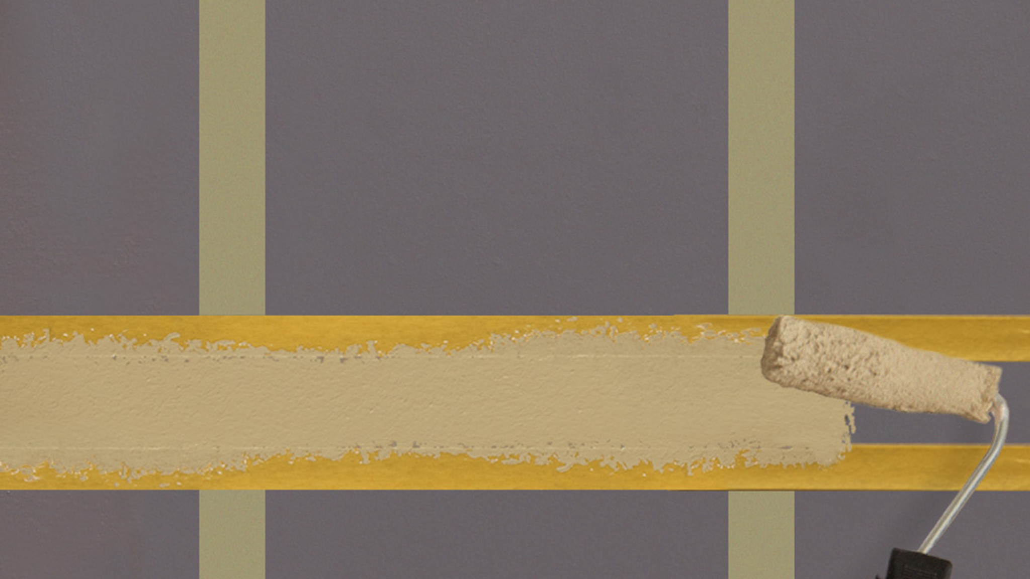 Someone applying paint with a smaller roller inside two horizontal strips of masking tape